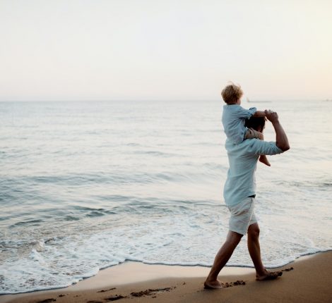 Father with a toddler boy walking on beach on summer holiday, having fun.